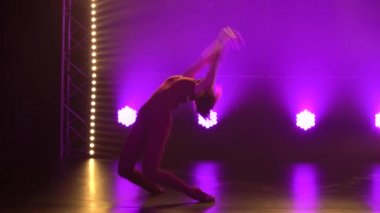 Esnek profesyonel bir bayan atlet, ritmik jimnastiğin karmaşık akrobatik unsurlarını sergiler. Neon ışıkları olan karanlık bir stüdyoda çekilmiş. Siluet. Kapat..