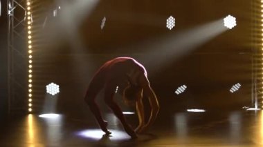 Esnek profesyonel bir bayan atlet, ritmik jimnastiğin karmaşık akrobatik unsurlarını sergiler. Neon ışıkları olan karanlık bir stüdyoda çekilmiş. Siluet. Kapat..