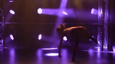 Esnek profesyonel bir bayan atlet, ritmik jimnastiğin karmaşık akrobatik unsurlarını sergiler. Neon ışıkları olan karanlık bir stüdyoda çekilmiş. Siluet. Kapat..