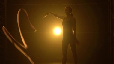 Ritmik jimnastik. Kameranın önünde dönen güzel, zarif jimnastik kurdelesi. Stüdyoda duman ve sarı ışıkla antrenman. Kapat..