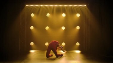 Sporcu kız jimnastikçi kız topla akrobatik egzersizler yapıyor ve esneme hareketleri yapıyor, vücudunun esnekliğini gösteriyor. Neon ışıkları olan karanlık bir stüdyoda çekilmiş. Yavaş çekim.