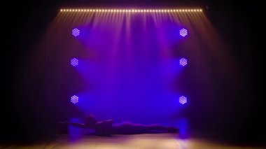 Mor spot ışıklarının altında, genç bir jimnastikçi bir topla akrobatik egzersizler yapıyor. Sıska, çekici bir kızın silüeti. Dar bir spor ceket içinde. Yavaş çekim.