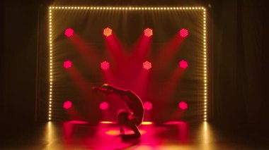 Esmer genç kadınlar ritmik jimnastik dansı yapıyor. Kırmızı spot ışıklarının arka planında siluetler. Yavaş çekim.