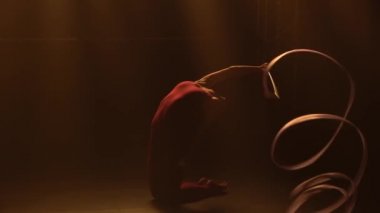 Ritmik jimnastik. Kameranın önünde dönen güzel, zarif jimnastik kurdelesi. Stüdyoda duman ve sarı ışıkla antrenman. Ağır çekim. Kapat..