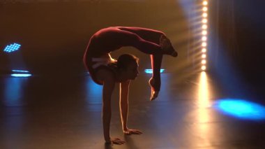 Sıkı spor kıyafetleri içinde bir jimnastikçi kız jimnastik elementleri sergiliyor ve harika bir esneme hareketi sergiliyor. Siluet. Ağır çekim. Kapat..