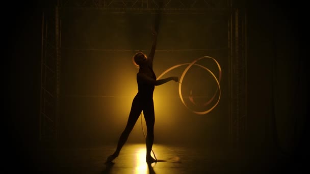 Rhythmische Sportgymnastik. Schöne anmutige Gymnastikbänder, die vor der Kamera spinnen. Training im Studio mit Rauch und gelbem weichen Licht. Zeitlupe. — Stockvideo