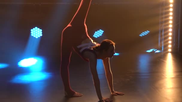 En flicka gymnast i en tight sport bodysuit utför gymnastik element och visar en underbar sträcka. Silhuett. Sakta i backarna. Närbild. — Stockvideo