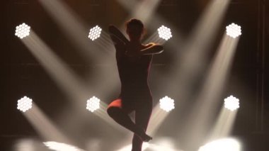 Odaklanmış genç jimnastikçi kız sahneye çıkmaya hazırlanıyor. Esneme egzersizleri yapıyorum. Kadın fitness. Spor yaşam tarzı. Arka planda spot ışıkları olan karanlık bir stüdyo. Kapatın. Yavaş çekim.