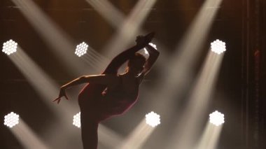 Odaklanmış genç jimnastikçi kız sahneye çıkmaya hazırlanıyor. Esneme egzersizleri yapıyorum. Kadın fitness. Spor yaşam tarzı. Arka planda spot ışıkları olan karanlık bir stüdyo. Kapatın. Yavaş çekim.
