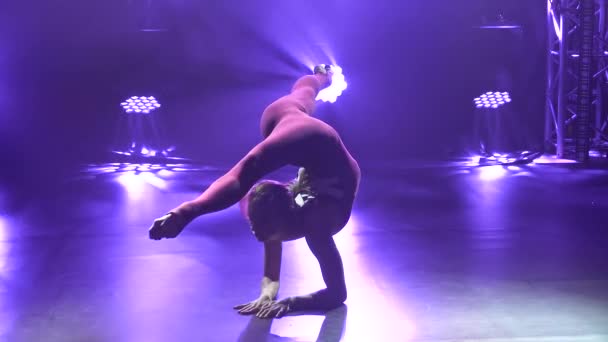 Slim athlète féminine professionnelle flexible effectue des éléments acrobatiques complexes de la gymnastique rythmique. Tourné dans un studio sombre avec des néons violets. Silhouette. Ferme là. Mouvement lent. — Video