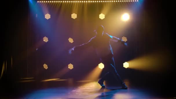 Knappe jongeman dansend breakdance, hiphop, straatdansen in de studio, geïsoleerd. Schot in de studio tegen een zwarte achtergrond met dynamische neon lichten. Silhouet. Langzame beweging. — Stockvideo