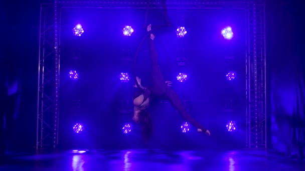 Chica joven silueta realiza los elementos acrobáticos en el anillo de aire. Grabado en un estudio oscuro con luces de neón azul en el fondo. Movimiento lento. — Vídeos de Stock