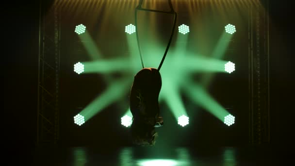 Giovane donna che fa spettacolo acrobatico trucco sul cerchio aereo. Emozionante spettacolo acrobatico in uno studio buio con illuminazione scenica verde. Silhouette di un corpo magro. Rallentatore. — Video Stock