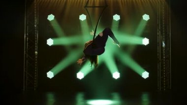 Genç bir kadın hava çemberinde akrobatik numaralar yapıyor. Karanlık bir stüdyoda yeşil sahne ışıklandırmasıyla heyecan verici bir akrobatik gösteri. İnce bir vücudun silueti. Yavaş çekim.