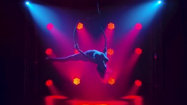 Güzel bir hava jimnastikçisi bir hava çemberinde baş aşağı asılı ve sicim yapıyor. Karanlık bir stüdyoda, üzerinde kırmızı ışık olan ince bir vücudun silueti. Yavaş çekim.