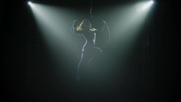Sport antenn akrobatik på höjden av bågen. Silhuett av en smal kropp i trånga trikåer. Föreställning i en mörk studio med scenbelysning. Långsamma rörelser. — Stockvideo