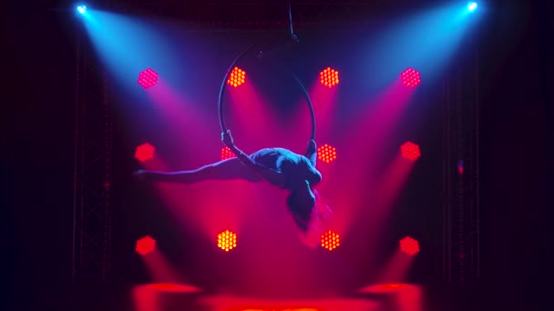Beautiful aerial gymnast hanging upside down on an air hoop and doing a twine. Silhouette of a slim body in a dark studio with red lighting. Slow motion. — Stock Video