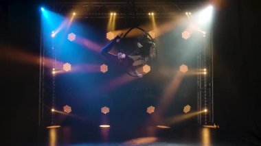 Esnek aerialn jimnastikçisi dairede döner ve havada akrobatik hareketler yapar. Karanlık bir stüdyoda arka planda neon ışıkları olan genç bir kız. Yavaş çekim.