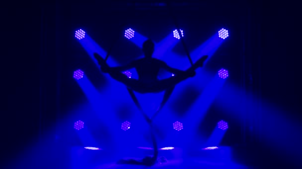 Vrouwelijke gymnaste draait en bindt op een rode zijde. Spannende acrobatische show. Donkere rokerige achtergrond en blauwe neon lichteffecten. Langzame beweging. — Stockvideo