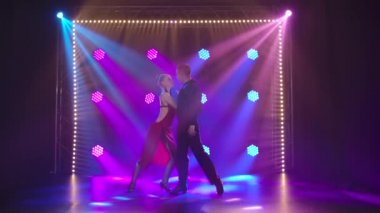 Etkileyici bir çift tarafından yapılan tutkulu tango dansı. Açık kırmızı elbiseli, derin yarıklı bir kadın ve siyah takım elbiseli bir adam. Sihirli ışıkları olan bir stüdyoda çekilmiş. Yavaş çekim.