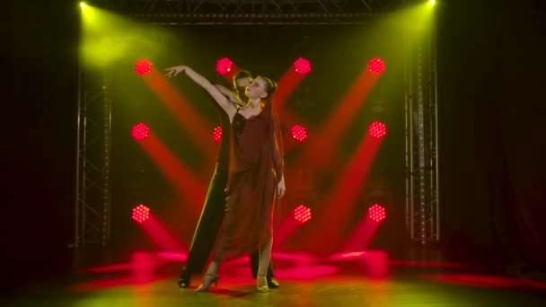 Ein romantisches Paar von Standardtänzern tanzt im Studio vor dem Hintergrund roter Scheinwerfer. Zeitlupe. — Stockvideo