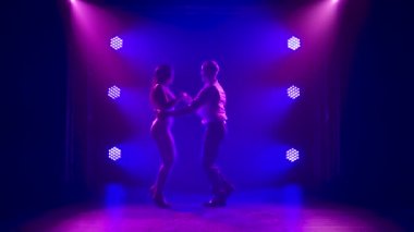 Dans eden genç çift Latin müziği. Bachata, merengue, salsa. Arka planda neon ışıkları olan karanlık bir stüdyoda çekilmiş..
