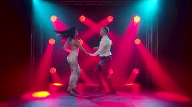 Dans eden genç çift Latin müziği. Bachata, merengue, salsa. Arka planda neon ışıkları olan karanlık bir stüdyoda çekilmiş..