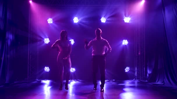 Casal jovem dançando música latina. Bachata, merengue, salsa. Filmado em um estúdio escuro com luzes de néon no fundo. — Vídeo de Stock