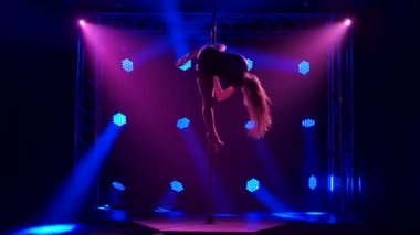 Erotik iç çamaşırlı bir striptizci direğin üzerinde döner ve sicim yapar. Karanlık bir stüdyoda mavi dinamik ışıkları olan bir kadının silueti..