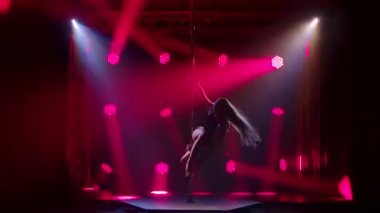 Mayo ve yüksek topuklu mayoyla seksi esmer, direkte dönüşümlü hareketler yapıyor. Alacakaranlıkta ve parlak kırmızı ışıklarda bir gece kulübünde gösteri yapmak. Siluet.