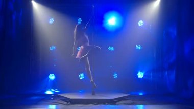 Mavi neon arka planda genç ve çekici bir kadın direğin üzerinde dans ediyor ve sonra bir öpücük yolluyor. Siluet.