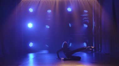 Çoraplı seksi kadın striptiz dansı yapıyor, plastikleri çıkartıyor. Siyah arka planda mavi spot ışıklarıyla hareket eden şehvetli sarışının silueti. Yavaş çekim.