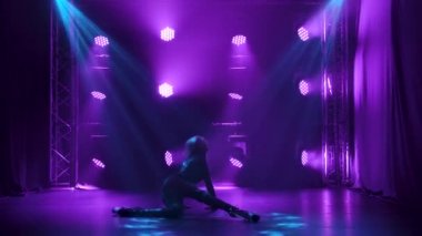 Seksi bir kadın dansçı erotik danslar yapar, striptiz yapar. Yüksek topuklu uzun bacaklı bir sarışının silüeti. Stüdyoda mor dumanlı arka plan. Yavaş çekim.