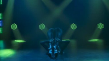 A young adult woman erotically touches her ass and spreads her legs wide performing elements of strip plastics. Seductive silhouette in tight black clothes and heels. Slow motion. Close up.