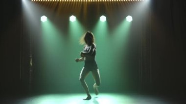 Spot ışıklarıyla modern dans eden bir kadın. Vogue ya da modern dans. Genç dansçı karanlık sahnede oynuyor..