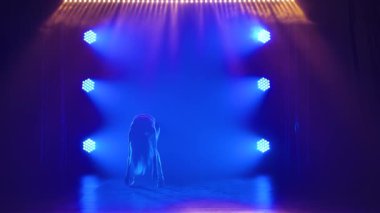 Spot ışıklarıyla modern dans eden bir kadın. Vogue ya da modern dans. Genç dansçı karanlık sahnede oynuyor..