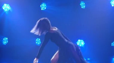Spot ışıklarıyla modern dans eden bir kadın. Vogue ya da modern dans. Genç dansçı karanlık sahnede oynuyor..