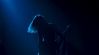 Spot ışıklarıyla modern dans eden bir kadın. Vogue ya da modern dans. Genç dansçı karanlık sahnede oynuyor..