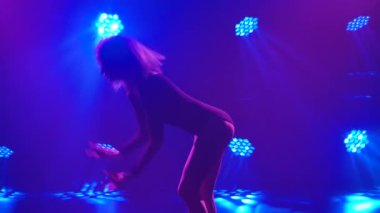 Spot ışıklarıyla modern dans eden bir kadın. Vogue ya da modern dans. Genç dansçı karanlık sahnede oynuyor..