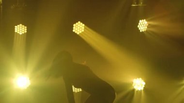 Spot ışıklarıyla modern dans eden bir kadın. Vogue ya da modern dans. Genç dansçı karanlık sahnede oynuyor..