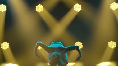 Spot ışıklarıyla modern dans eden bir kadın. Vogue ya da modern dans. Genç dansçı karanlık sahnede oynuyor..