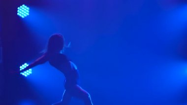 Spot ışıklarıyla modern dans eden bir kadın. Vogue ya da modern dans. Genç dansçı karanlık sahnede oynuyor..