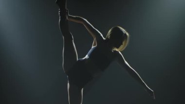 Spot ışıklarıyla modern dans eden bir kadın. Vogue ya da modern dans. Genç dansçı karanlık sahnede oynuyor..