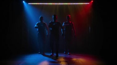 Bir grup akrobat erkek jimnastikçi akrobatik egzersizler serisi yapıyorlar. Siyah bir arka planda sahne ışıkları altında. Yavaş çekim.