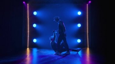 Bir grup erkek jimnastikçi dengeyi sağlamak için akrobatik hareketler sergiliyor. Siyah arka planda spot ışıkları olan iki adamın siluetleri. Yavaş çekim.