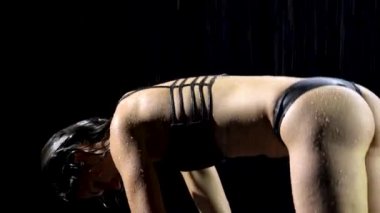 Koyu saçlı güzel bir kadın yoga egzersizleri yapıyor. Yağmur damlasıyla ıslanan kadın, yoga yaparken esneme hareketleri ve asma egzersizleri yapar. Yağmurlu bir havada karanlık bir stüdyoda çekildi. Siyah arka plan. Kapat.