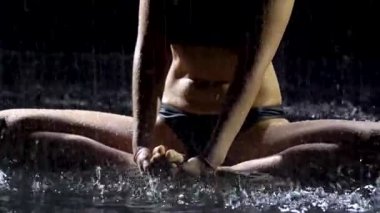 Yağmurda kalmış genç bir kadın asanas dansı yaparak yoga yapıyor. Yağmur damlalarında sıkılaşmış kadın vücudu. Resim stüdyoda siyah bir arkaplanda çekildi. Kapat..