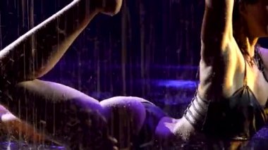 Yağmurdan ıslanmış ince bir kadın karanlık bir stüdyoda yoga yapıyor. Seksi vücut stüdyo ışıklarında parlayan su damlacıklarıyla kaplıdır. Siyah arka plan. Kapat..