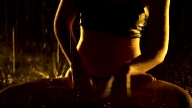 Yağmurdan ıslanmış siluet gibi ince bir kadın karanlık bir stüdyoda yoga yapıyor. Seksi vücut stüdyo sarı ışıkta parlayan su damlacıklarıyla kaplıdır. Siyah arka plan. Kapat..