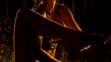 Yağmurdan ıslanmış siluet gibi ince bir kadın karanlık bir stüdyoda yoga yapıyor. Seksi vücut stüdyo sarı ışıkta parlayan su damlacıklarıyla kaplıdır. Siyah arka plan. Kapat..